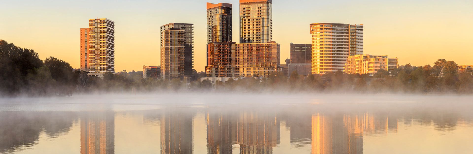 The Canberra skyline at sunrise, city towers reflected in mist