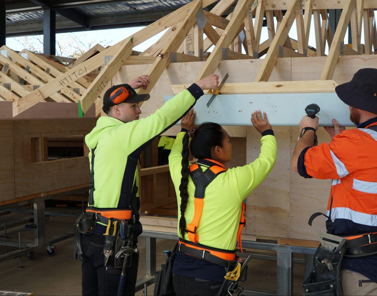 Three workers in hi-vis reaching up to fix overhead timber framing