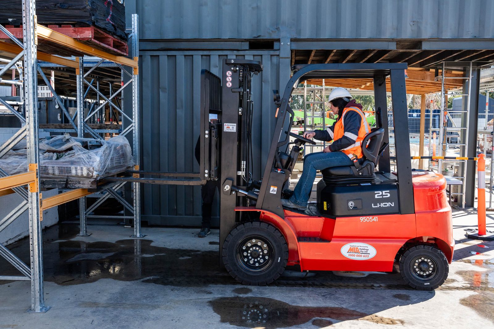 Worker in orange hi-vis driving a forklift down a warehouse racking aisle