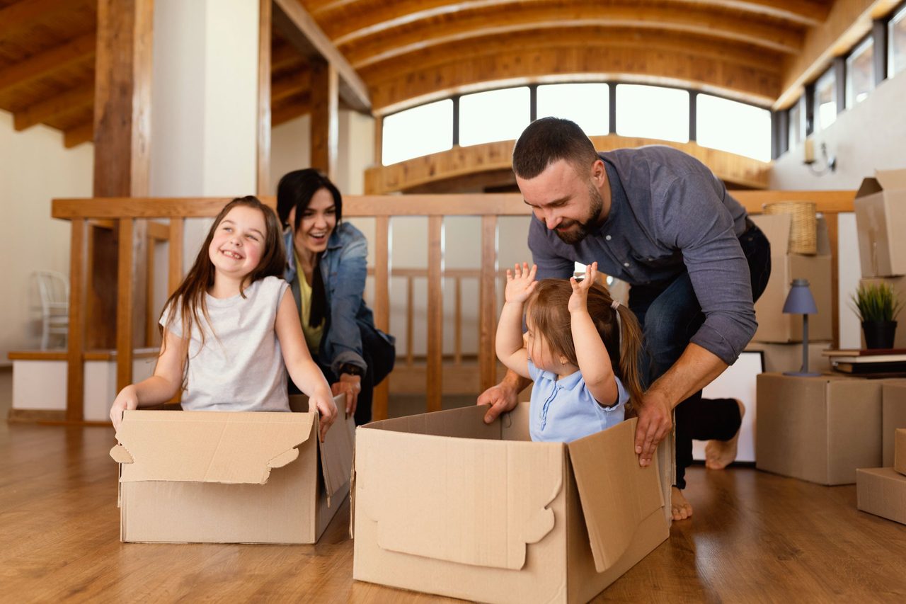 A family with young children unpacking moving boxes in their new home under exposed timber beams.
