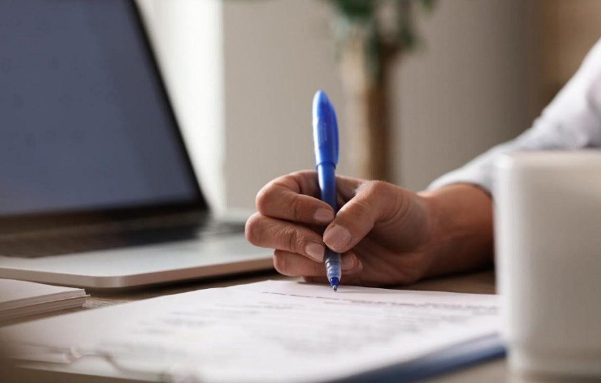 A hand holding a pen over a document on an office desk.