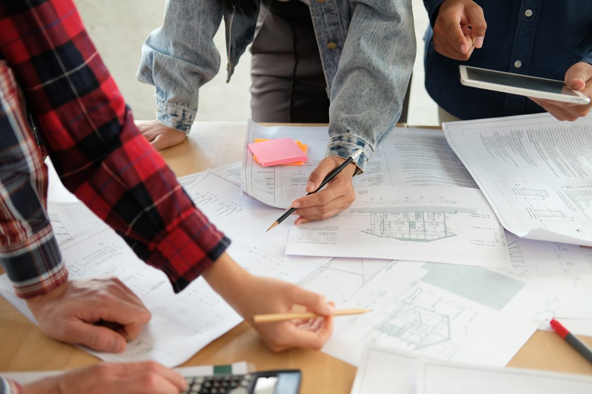Three people reviewing architectural plans together at a table, marking them up with pens.