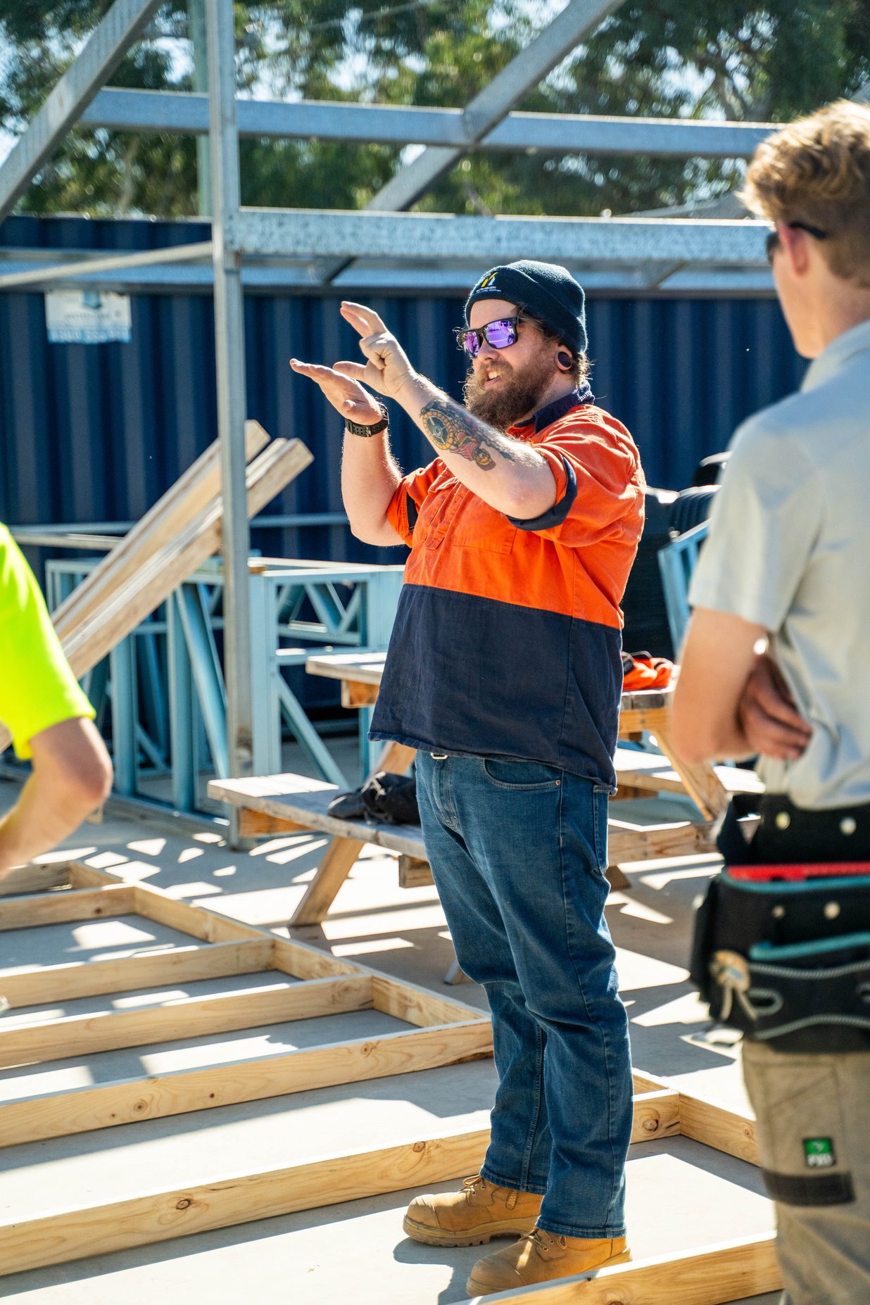 A construction worker in a high-visibility shirt and cap talking with colleagues on a building site.