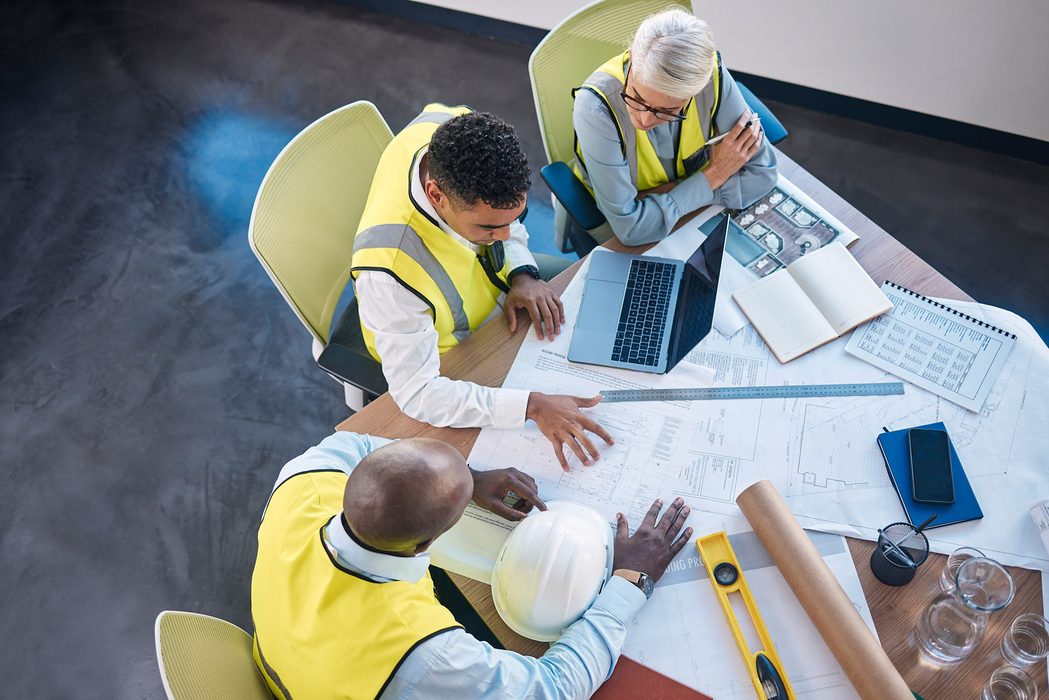 A team meeting around a laptop and building plans in an office.