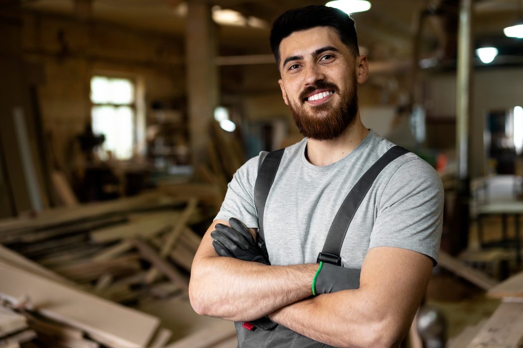A smiling construction worker with arms crossed in a workshop.