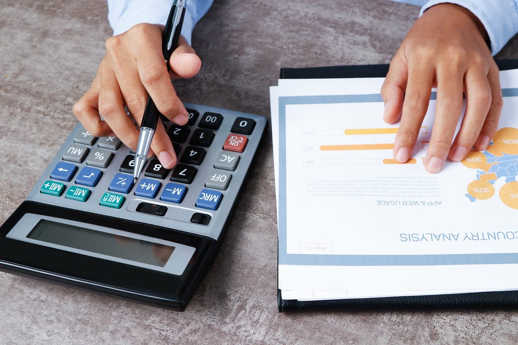 Hands on a calculator beside financial documents and charts.