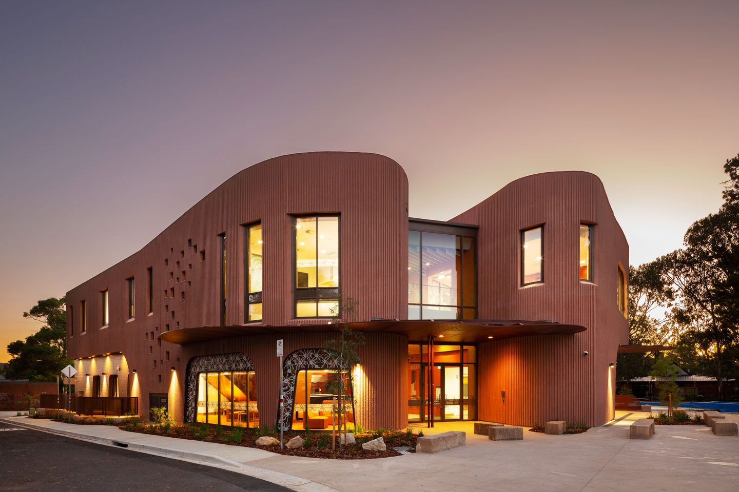 A curved commercial building with a corrugated metal facade lit at dusk