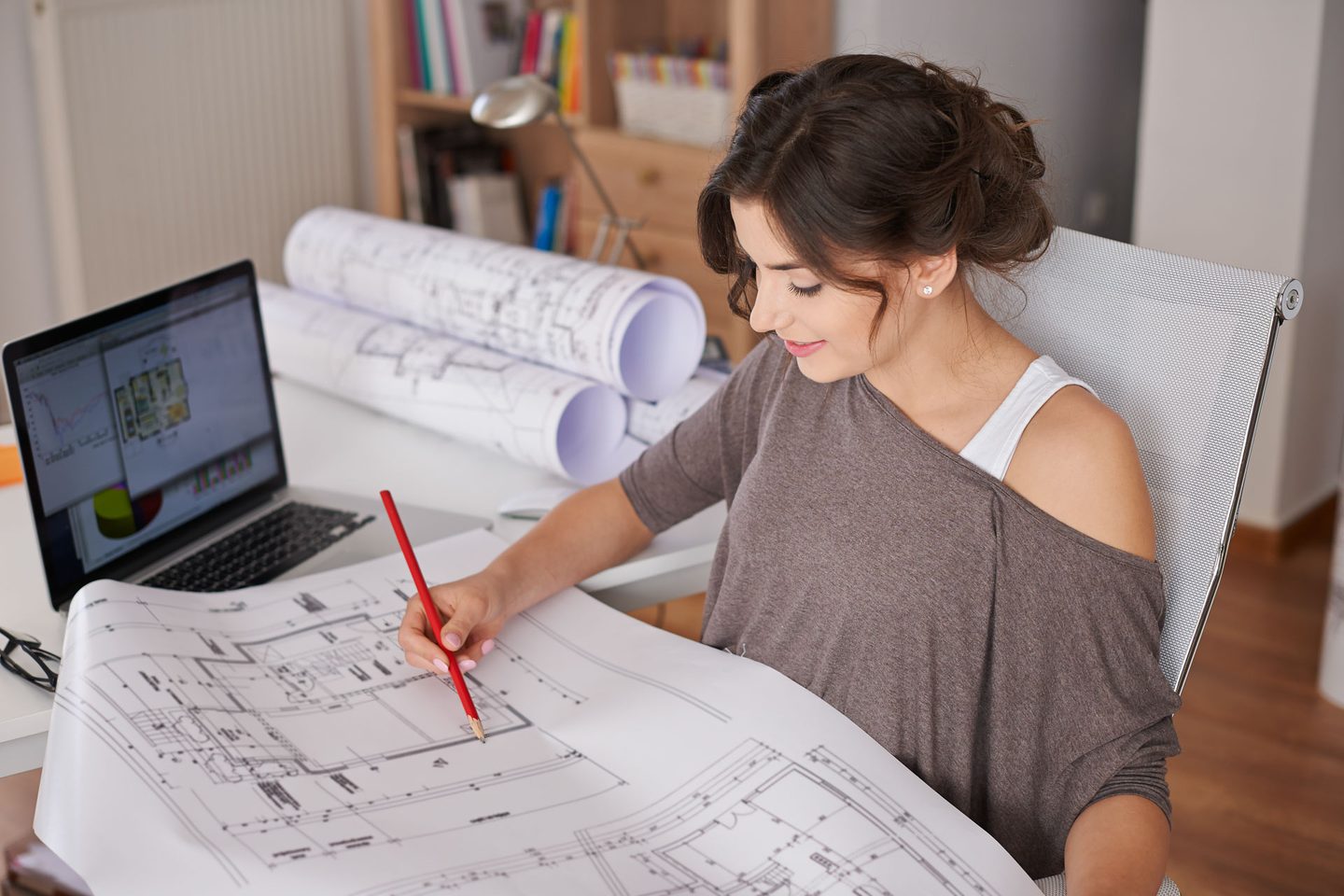 An architect reviewing building plans at a desk with a laptop