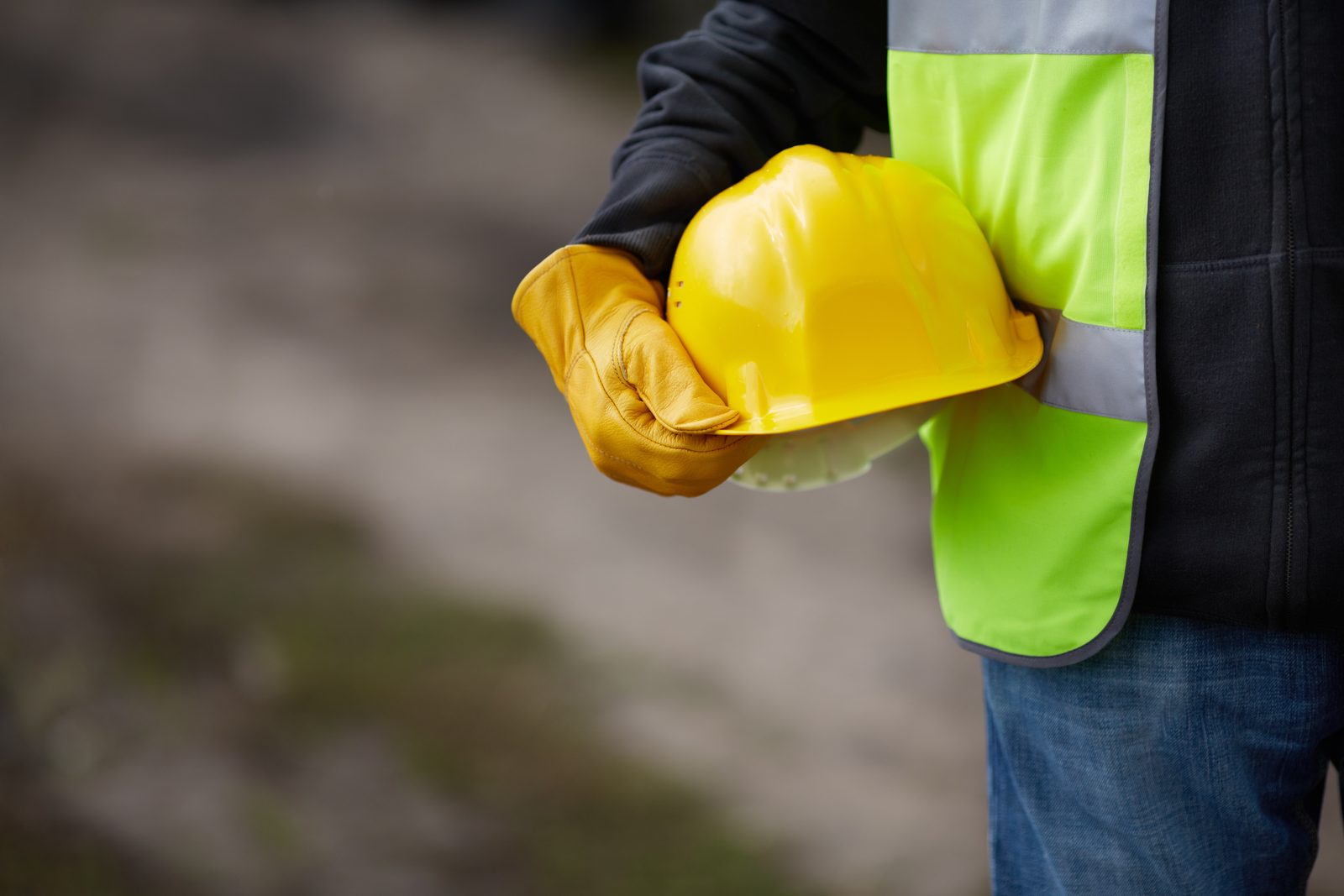 Worker in safety vest holding yellow hard hat