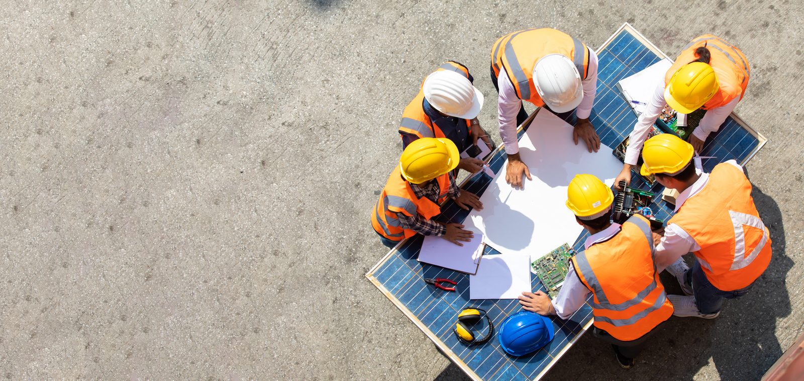 Construction workers in hard hats around solar panels reviewing plans