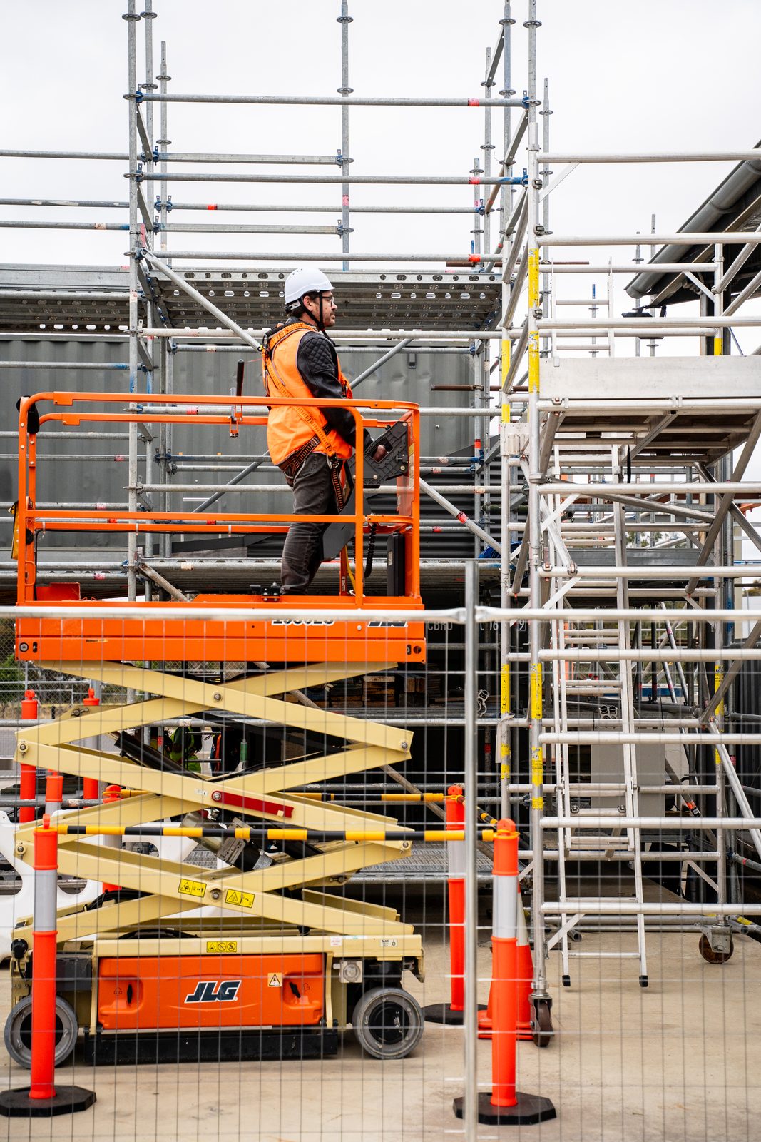 Worker standing on orange elevated scissor lift platform with metal construction scaffolding in background