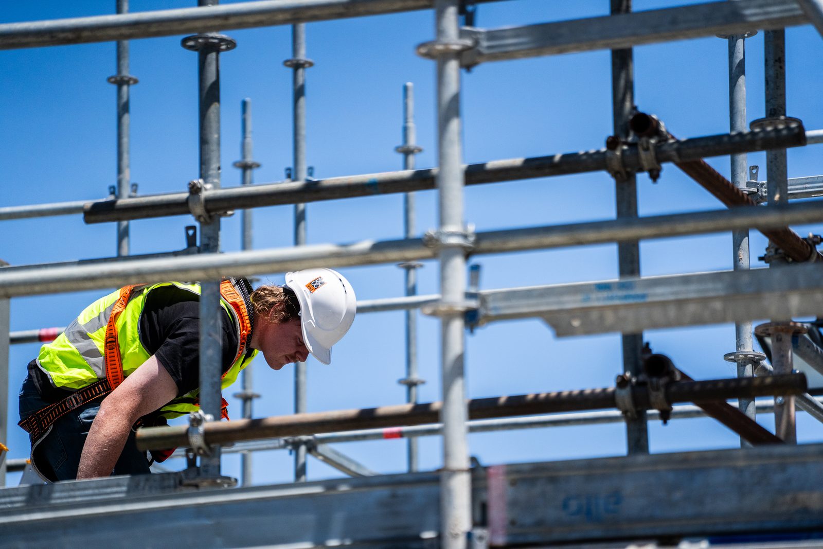 Worker in safety harness securing metal scaffolding framework at elevated height